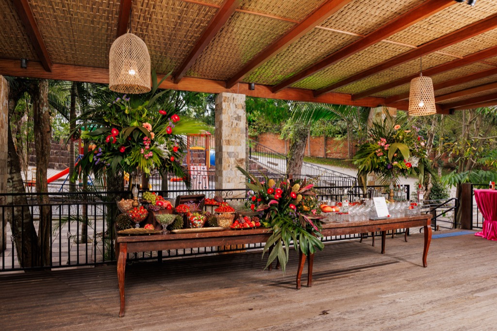 Deck coberto na Chácara do Cris — mesa de buffet com frutas e flores tropicais