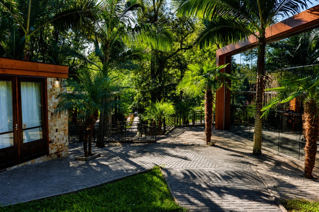 Fachada da Chácara do Cris — área externa com vidro, pedra e palmeiras